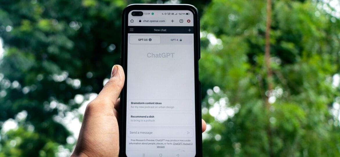 A hand holds a phone with the "ChatGPT" site on the screen.