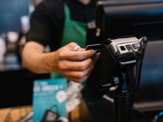 A retail worker handles a transaction in front of a kiosk. (Photo by Anna Tarazevich).