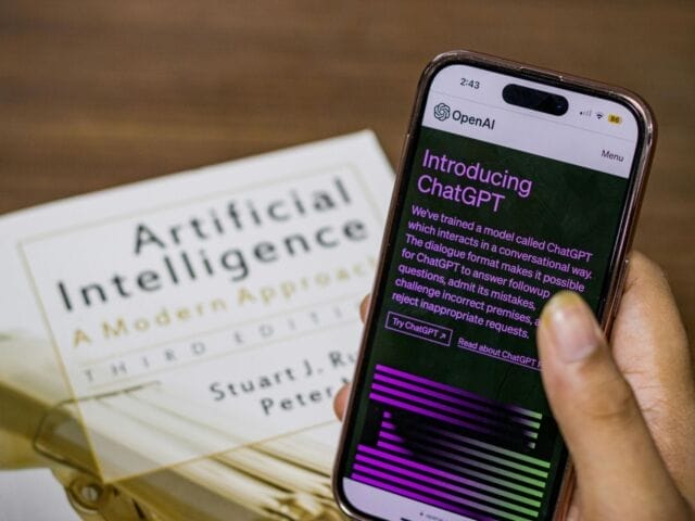 An Artificial Intelligence publication and a hand holding a phone with "ChatGPT" on the screen.