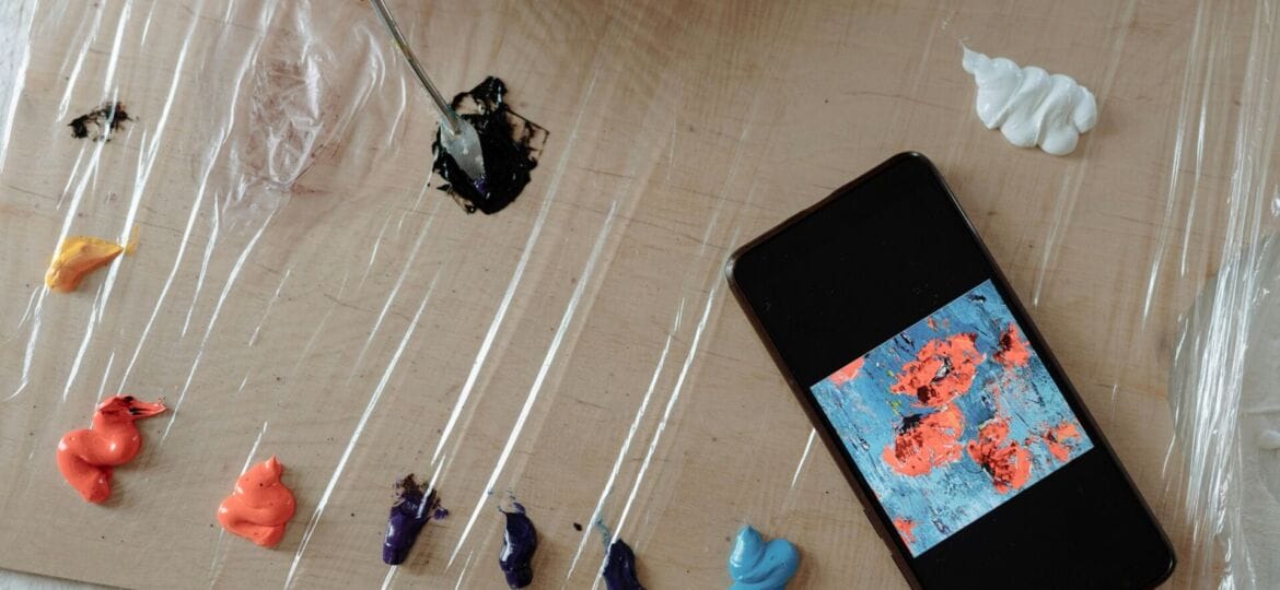 A phone and several paint colors sit on a brown surface.